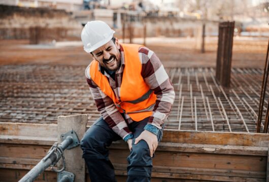 A builder is sitting on concrete foundation and screaming in pain. He injured his leg.