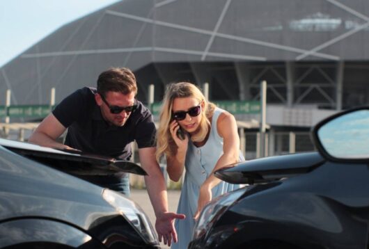 Woman driver using smartphone to call. Man driver looking on smashed broken car in accident