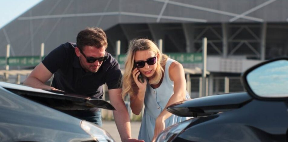 Woman driver using smartphone to call. Man driver looking on smashed broken car in accident